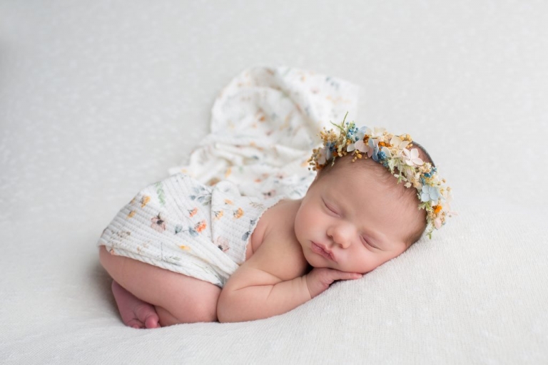 Newborn girl less than 2 weeks old wearing a handmade flower crown on a white backdrop, taken on a beanbag